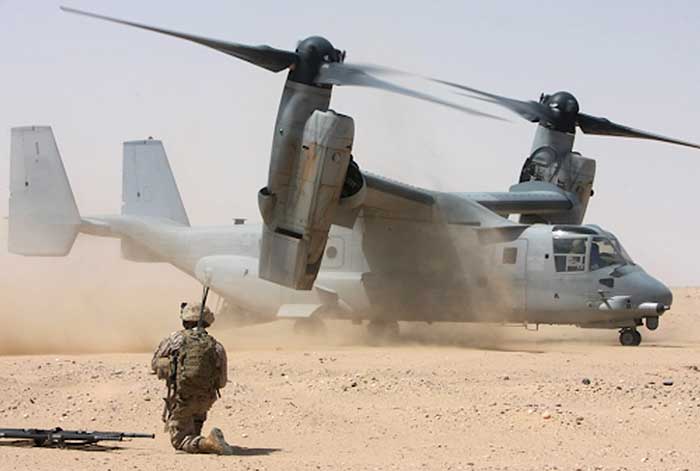 Service member kneeling in front of an airplane in the desert